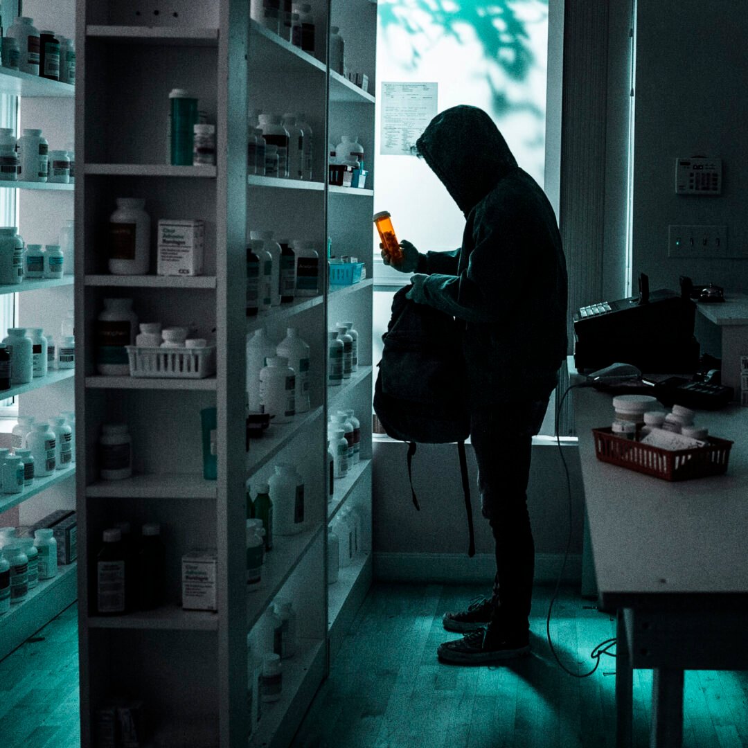 Person in dark hoodie holding medicine bottle
