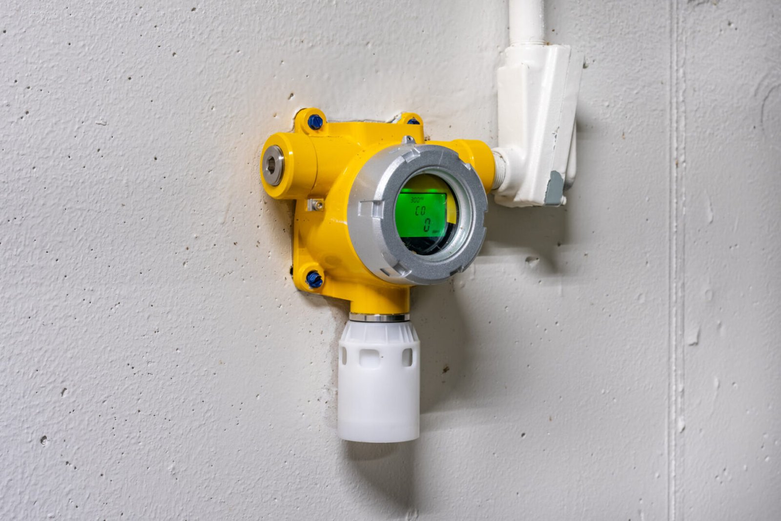 Yellow gas detector sensor mounted on a wall with white piping.